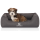 Ein kleiner, flauschiger Hund sitzt bequem in einem grauen Haustierbett, auf dem das Logo "KNUFFELWUFFF" deutlich sichtbar ist.