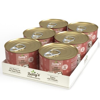 Sechs Dosen von Betty's Landhausküche Hundefutter, mit einem rosa Etikett mit einem Cartoon-Hund, das "Wild & Geflügel" und "Extra viel Fleisch" angibt.