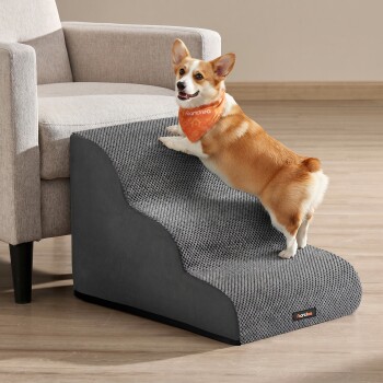 Corgi klettert eine grau strukturierte Haustierrampe zur Couch hinauf, trägt ein oranges Bandana mit weißem Text und einem kleinen schwarzen Produktschild.