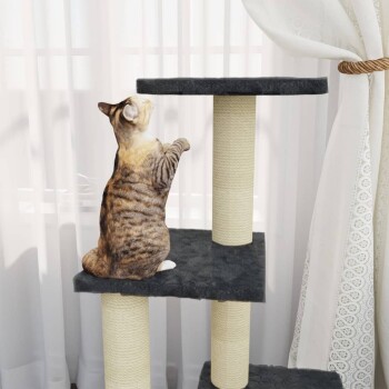Eine verspielte getigerte Katze steht auf einem mehrstöckigen Katzenbaum und greift nach der obersten Plattform, mit durchsichtigen Vorhängen im Hintergrund.
