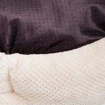 Ein plüschiges Hundebett mit einem dunklen, gepunkteten Stoff oben und einem weichen, cremefarbenen Fleeceboden.