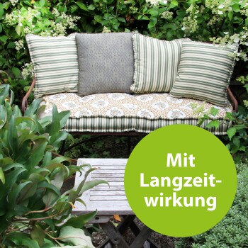 Eine Gartenbank mit gemusterten Kissen und drei Kissen, umgeben von Grün, mit einem runden Etikett, das "Mit Langzeitwirkung" sagt.
