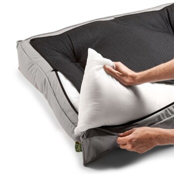 Eine Person passt ein Haustierbett mit abnehmbarem Bezug an, hält ein weißes Kissen und öffnet den schwarzen gepunkteten oberen Teil.