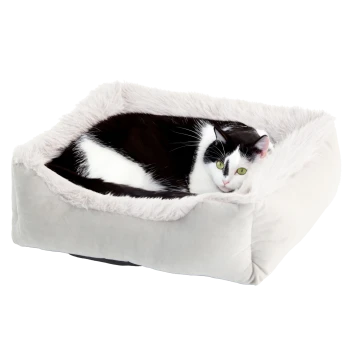 Eine schwarz-weiße Katze, die in einem plüschigen, quadratischen Haustierbett mit einem weichen, flauschigen Rand entspannt, vor einem weißen Hintergrund.