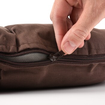 Eine Nahaufnahme einer Hand, die ein braunes Haustierbett aufzippt, das den strukturierten Stoff und das Reißverschlussdetail zeigt.