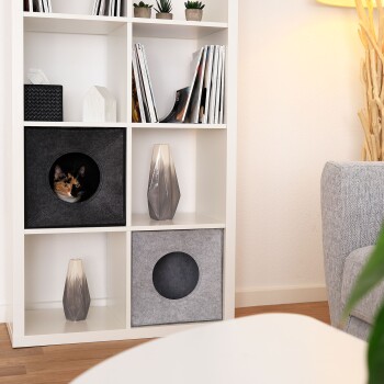 Ein moderner weißer Bücherregal mit dekorativen Gegenständen, darunter Topfpflanzen, Zeitschriften und zwei stilvolle Vasen, eine grau und eine klar.