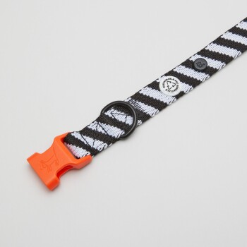 Schwarz-weiße gestreifte Hundeleine mit einer orangefarbenen Schnalle und einem schwarzen Metallring, mit einem Nachhaltigkeitsabzeichen.