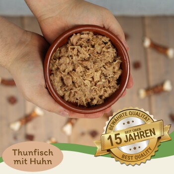 Eine Person hält eine braune Schüssel mit zerkleinertem Thunfisch und Huhn, mit einem Abzeichen, das "Beste Qualität" und "15 Jahre" auf Deutsch angibt.