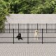 Zwei Hunde, ein schwarzer Labrador und ein gelber Labrador, stehen hinter einem schwarzen Metallzaun in einem gepflasterten Außenbereich, umgeben von Grün.