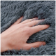 Eine Nahaufnahme einer Hand, die sanft in eine weiche, flauschige graue Haustierdecke drückt und deren plüschige Textur zeigt.