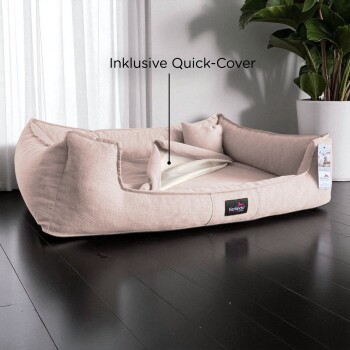 Beiges rechteckiges Haustierbett mit Kissen und inklusive Schnellbezug, auf dunklem Holzboden neben einer Pflanze platziert.