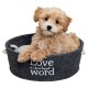 Un chiot tan duveteux se prélassant dans un lit pour animaux de compagnie gris rond avec le texte "L'amour est un mot à quatre pattes" imprimé sur le côté.