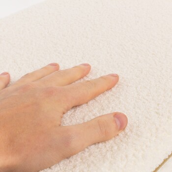 Eine Hand ruht auf einer weichen, flauschigen weißen Haustierbettoberfläche und zeigt deren plüschige Textur.