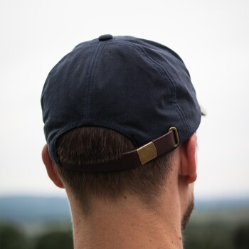 Mann trägt schwarze Baseballkappe mit Lederband, von hinten vor unscharfem Außenhintergrund gesehen.