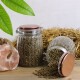 Zwei Glasbehälter mit braunen Tierpellets auf Holz und Heu, eines aufrecht und eines verschüttet, Kupferdeckel, grüne Blätter und Salzgestein.