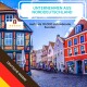 Bunte historische Gebäude säumen eine Kopfsteinpflasterstraße, mit Außenbestuhlung und einem Banner mit der Aufschrift 'Unternehmen aus Norddeutschland.'