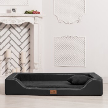 Stylisches schwarzes Haustierbett mit plüschigem Innenraum und kleinem Kissen, in einem hellen Raum mit einem dekorativen Kamin platziert.