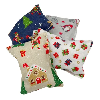 Quatre coussins pour animaux de compagnie de vacances : bleu avec des elfes, beige avec une maison en pain d'épice, blanc avec le Père Noël, et un à motifs avec des cadeaux colorés.
