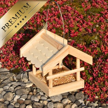 Holz-Vogelfutterspender mit einem geneigten Dach, gefüllt mit Samen, vor einem Hintergrund aus buntem Laub und Kieselsteinen, beschriftet mit "PREMIUM."