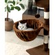 Eine flauschige graue Katze, die in einer gemütlichen braunen Hängematte an einem Katzenbaum entspannt, mit einer Topfpflanze und Möbeln im Hintergrund.