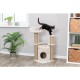 Eine schwarze Katze steht verspielt auf einem beigen Kratzbaum mit Kratzsäulen und einem gemütlichen Versteck, umgeben von Zimmerpflanzen und Regalen.
