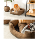 Ein flauschiger Pomeranian-Hund sitzt bequem in einem gemütlichen braunen Haustierbett mit einem weichen, hellen Innenraum, umgeben von einer Pflanze und einem dekorativen Regal.