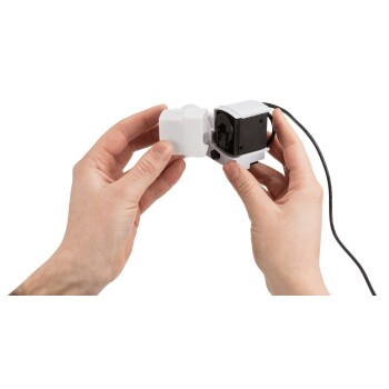 Die Hände einer Person halten ein kleines weißes und schwarzes Haustierprodukt, möglicherweise eine Pumpe oder einen Filter, mit einem schwarzen Stromkabel.