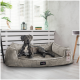 Ein grauer Hund ruht sich bequem auf einem plüschigen Hundebett in einem hellen Raum mit weißen Jalousien aus. Das Bett hat ein Etikett mit der Aufschrift 'tierlando'.