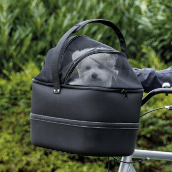 Ein kleiner weißer Hund schaut aus einer schwarzen Haustiertragetasche mit einem Netzoberteil, die an einem Fahrrad befestigt ist, vor einem grünen Hintergrund.