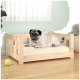Ein entspannter Mops liegt auf einem Holz-Haustierbett mit einem beigen Kissen, neben einem grünen Tennisball, in einem sanft beleuchteten Raum.
