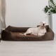Ein weißer Hund, der auf einem braunen Haustierbett in einem modernen Raum mit einer Pflanze und einer dekorativen Lampe im Hintergrund entspannt.