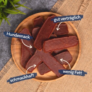 Ein Holzbrett hält mehrere Streifen Hundesnacks, beschriftet mit den Texten: "Hundesnack", "gut verträglich", "schmackhaft" und "wenig Fett."