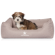 Ein kleiner, flauschiger Welpe mit braunem und weißem Fell sitzt bequem in einem beigen Hundebett, auf dem das Logo "KNUFFELWUFF" zu sehen ist.