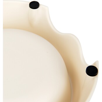 Eine Nahaufnahme einer beigen Futterschüssel für Haustiere mit gewelltem Rand und drei schwarzen Gummifüßen für Stabilität.