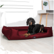 Ein schwarzer Dobermann liegt auf einem roten Hundebett mit einem Logo, das "tierlando" liest, vor einem Backsteinwand-Hintergrund.