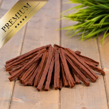 Premium-Hundeleckereien, die auf einer Holzoberfläche zu einem Haufen angeordnet sind, mit einem dekorativen Element aus grünem Gras im Hintergrund.