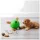 Ein flauschiger goldenes Welpe spielt mit einem grünen interaktiven Spielzeug, das wie ein Ball mit pelzigen Beinen aussieht, umgeben von verstreuten Hundeleckerlis.