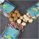 Verschiedene Haustierleckerlis auf einer dunklen Oberfläche präsentiert, einschließlich der Verpackungen 'Duo Pallinos' und 'Kokos Crunchies', mit verschiedenen Snacks in verschiedenen Formen verstreut.
