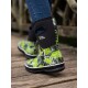 Nahaufnahme eines Beins einer Person, die lebhaft grüne und schwarze gemusterte wasserdichte Stiefel mit dem Logo "Two Tracks" trägt, auf Holzplanken stehend.
