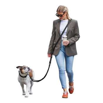 Frau in Blazer und Jeans geht mit einem braun-weißen Hund an der Leine spazieren und hält einen Reise-Kaffeebecher.