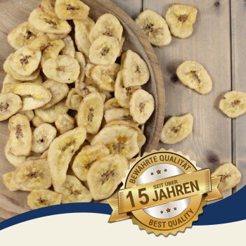 Getrocknete Bananenscheiben in einer Holzschale mit einem goldenen Abzeichen mit der Aufschrift "15 Jahren" und "Bewährte Qualität" auf einer Holzoberfläche.