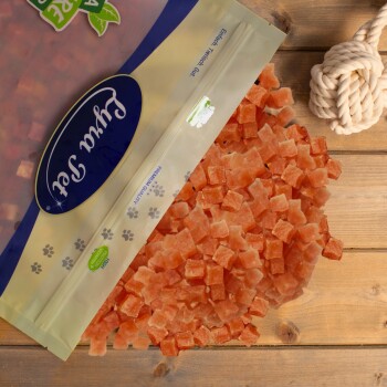 Eine Tüte gefriergetrockneter Katzenleckerlis mit kleinen, gewürfelten Stücken, die auf eine Holzoberfläche fallen, mit einem blauen Logo und einem Pfotenabdruckdesign.