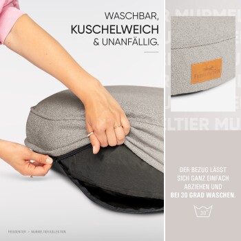 Eine Person öffnet einen grauen Bezug für ein Haustierbett, der mit 'Waschbar, kuschelig & pflegeleicht' beschriftet ist, mit Waschhinweisen für 30 Grad.
