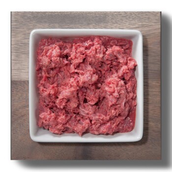 Ein quadratisches weißes Geschirr gefüllt mit rohem Hackfleisch, auf einer Holzoberfläche platziert.