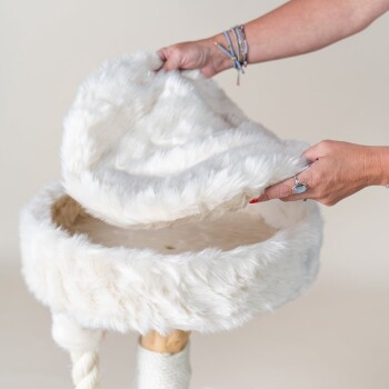 Die Hand einer Person hebt einen weichen, flauschigen weißen Haustierbettbezug an und zeigt das Innere des Bettes, das eine natürliche Holzunterlage hat.