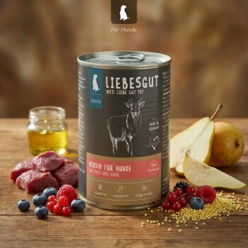 Dose Liebesgut Hundefutter mit der Aufschrift 'Hirsch für Hunde' und 'Sensitiv' sowie einer Hirsch-Illustration, umgeben von rohem Fleisch, Birne, Beeren, Öl und Hirse.