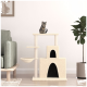 Eine verspielte getigerte Katze sitzt auf einem beigen Katzenbaum mit mehreren Ebenen und einem gemütlichen Versteck, neben einem grünen Sessel und einer Topfpflanze.