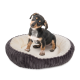 Ein kleiner Hund sitzt in einem plüschigen, runden Haustierbett mit einem dunkelgrauen Äußeren und einem weichen, cremefarbenen Inneren.
