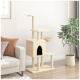 Ein beiger Katzenbaum mit mehreren Ebenen, einem gemütlichen Versteck und einer Schüssel, neben einem hellgrauen Sofa mit dekorativen Kissen und einer Topfpflanze.