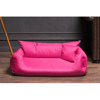 Helles pinkes Haustierbett mit zwei gepolsterten Seiten und einem weichen Boden, vor einer dunklen Wand und einem Holzboden.